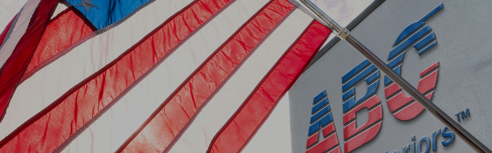 United States flag flying outside of a building with ABC Supply Interiors logo sign.