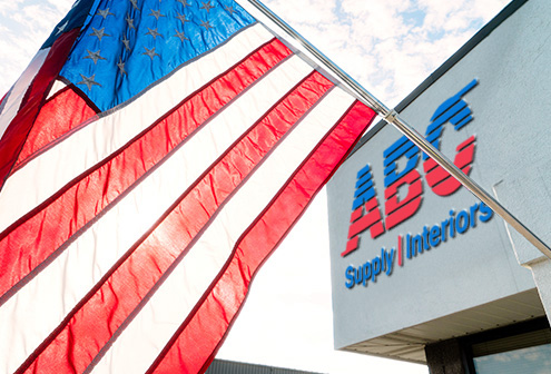 United States flag flying outside of a building with ABC Supply Interiors logo sign.